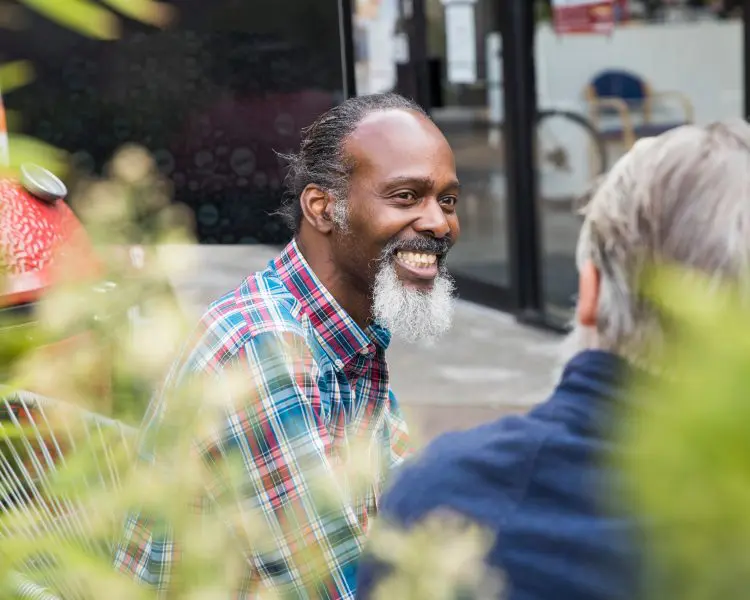 Man with grey beard smiling at another person