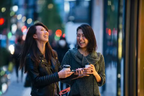 Two women laughing together holding coffee cups