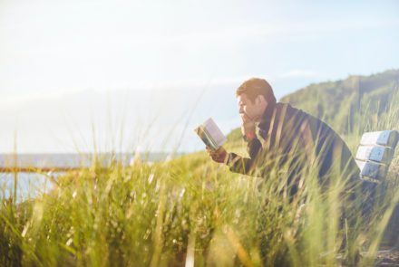 man reading book near some cliffs