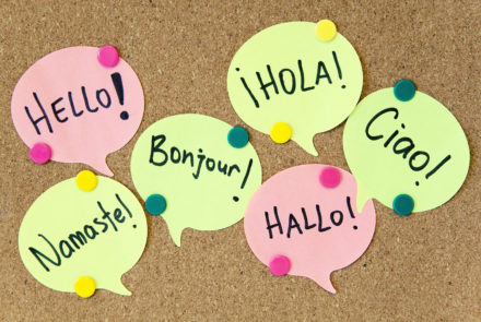 A cork board with paper speech bubbles pinned to it, saying 'hello' in different languages