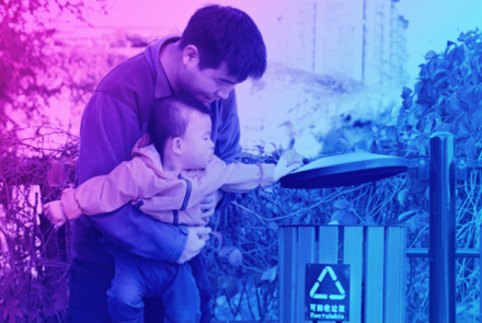 A father teaching his toddler son how to recycle with a recycling bin in a park