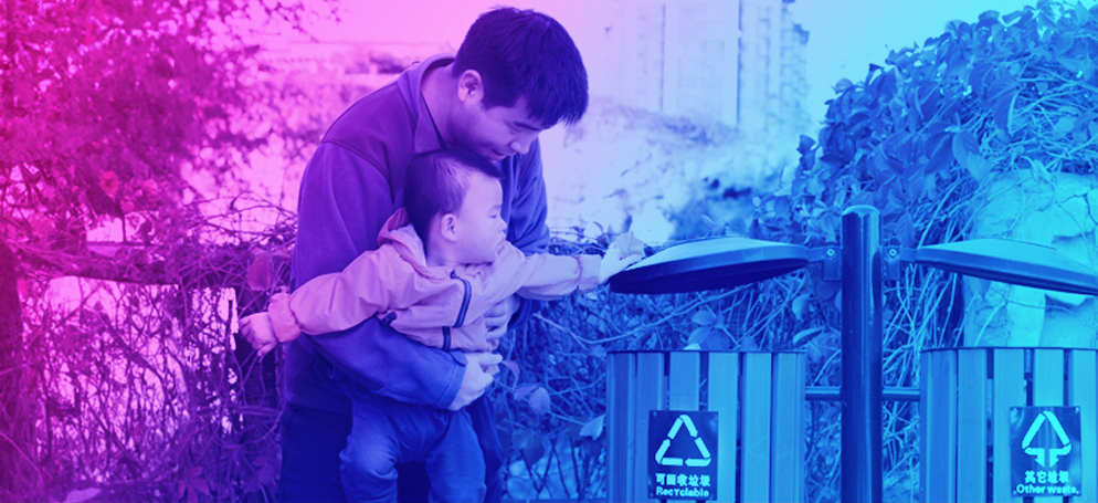 A father teaching his toddler son how to recycle with a recycling bin in a park