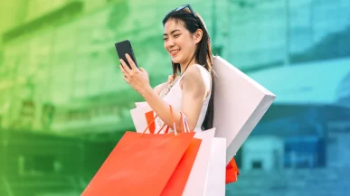 A woman checking her phone whilst carrying luxury shopping bags
