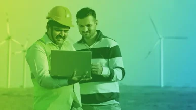 two men looking at laptop with wind turbines