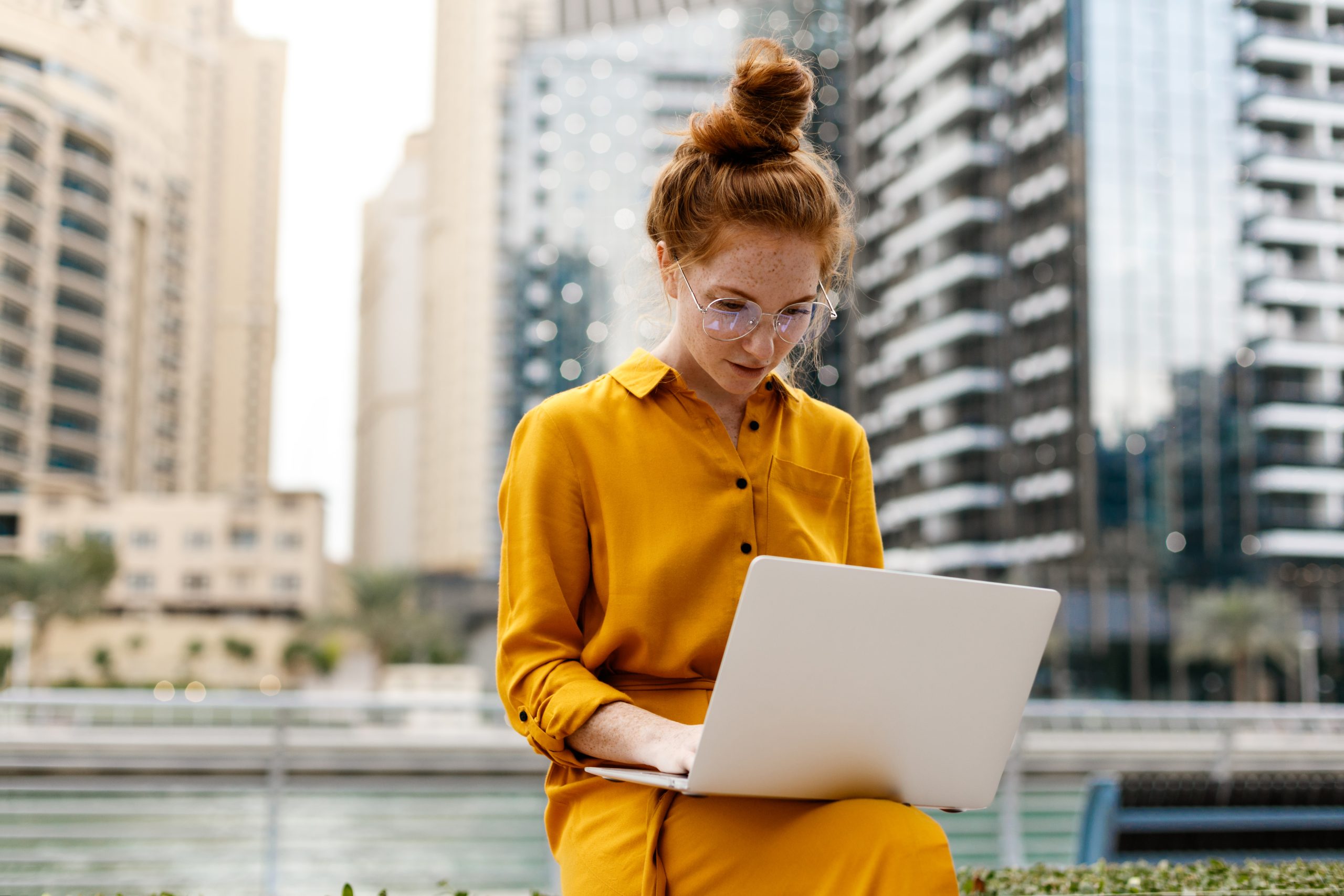A woman using a laptop in front of some skyscrapers.